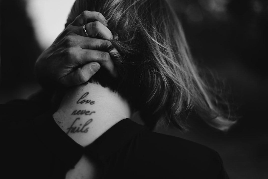 Tattoos and Mental Health: What the Research Actually Shows — grayscale photo of woman holding her neck while showing Love never Fails tattoo at back